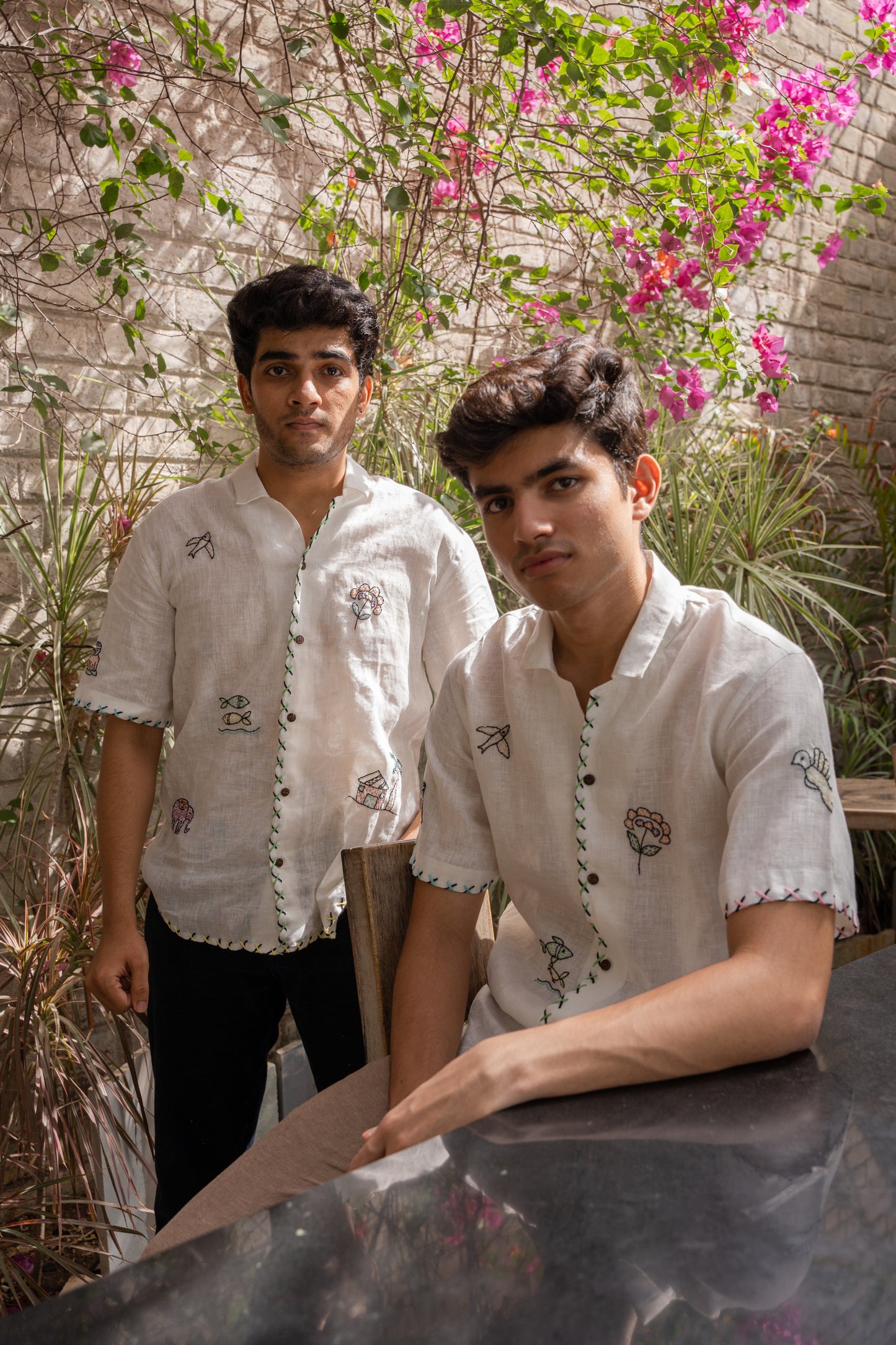 Two boys wearing the same white linen half-sleeve shirt with multiple motifs like elephants, birds, huts embroidered all over