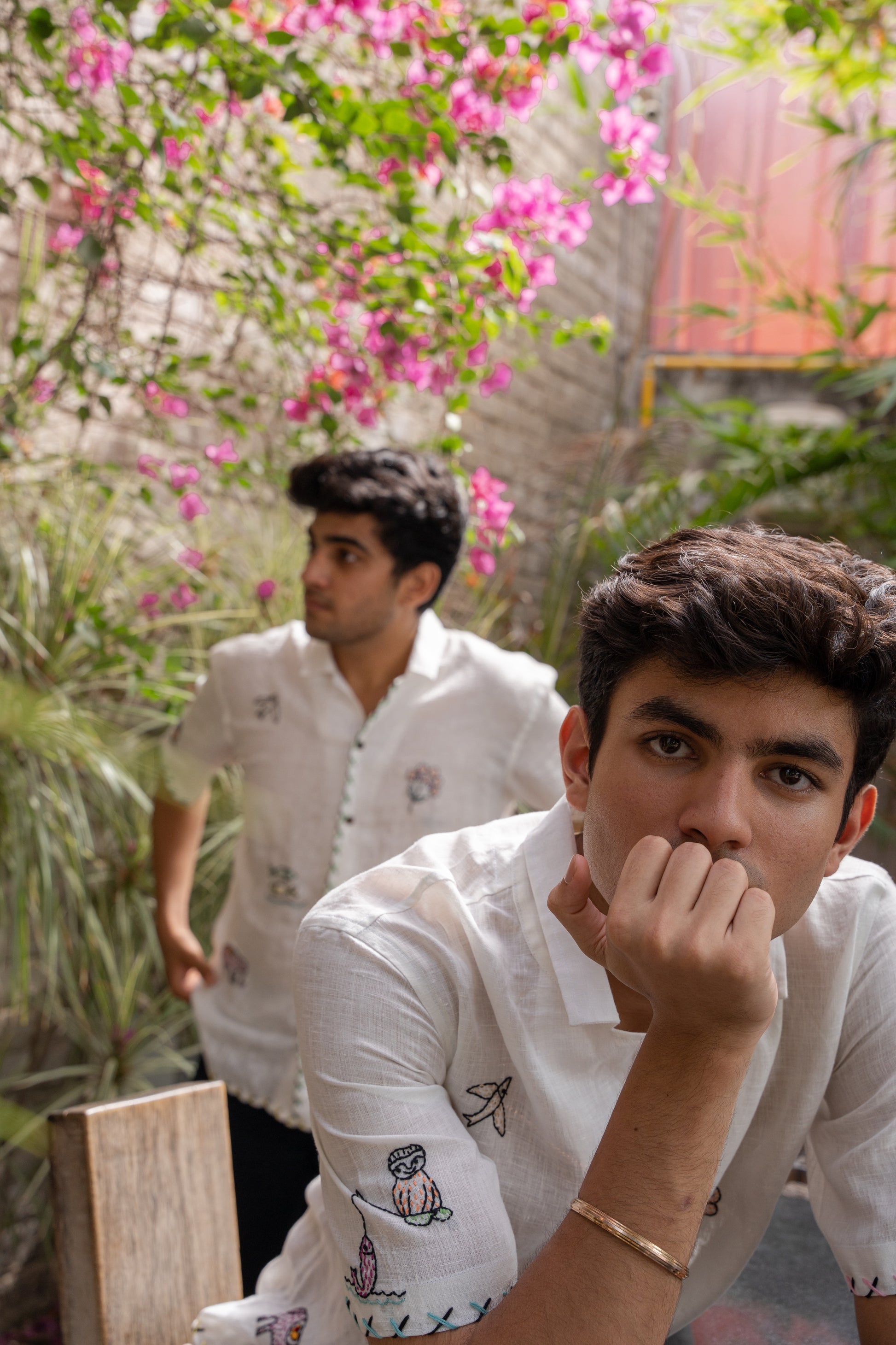 Two boys wearing the same white linen half-sleeve shirt with multiple motifs like elephants, birds, huts embroidered all over