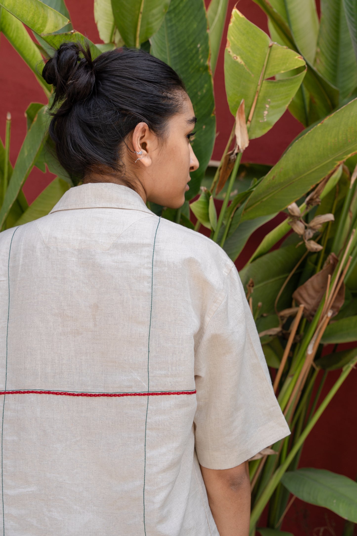 back of a girl in a beige linen shirt with horizontal and vertical embroidered lines in red and green