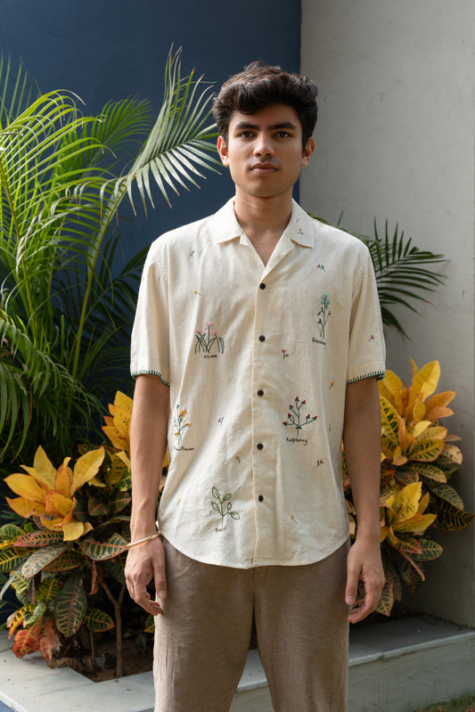 A young man in an off-white half sleeved shirt with stalks of beautiful herbs interspersed through the shirt