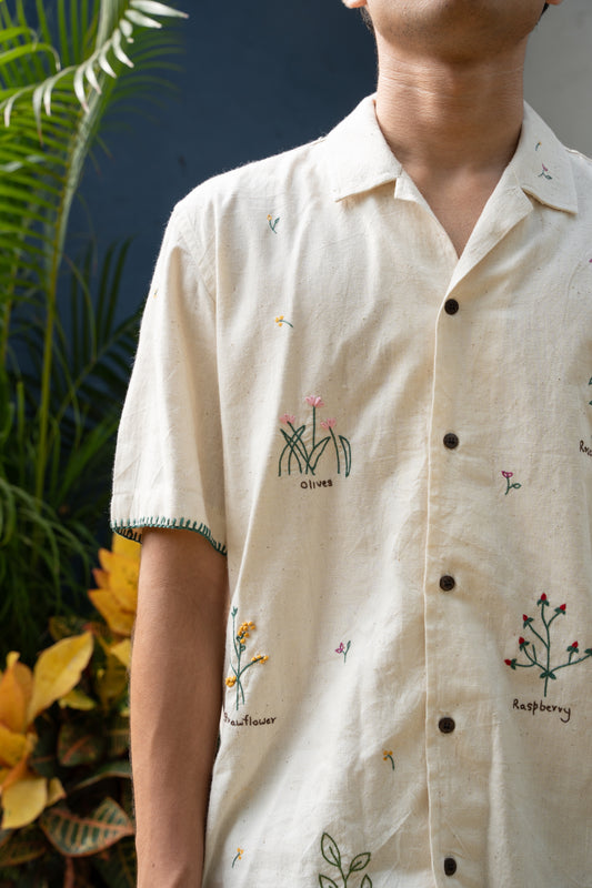 A young man in an off-white half sleeved shirt with stalks of beautiful herbs interspersed through the cotton shirt