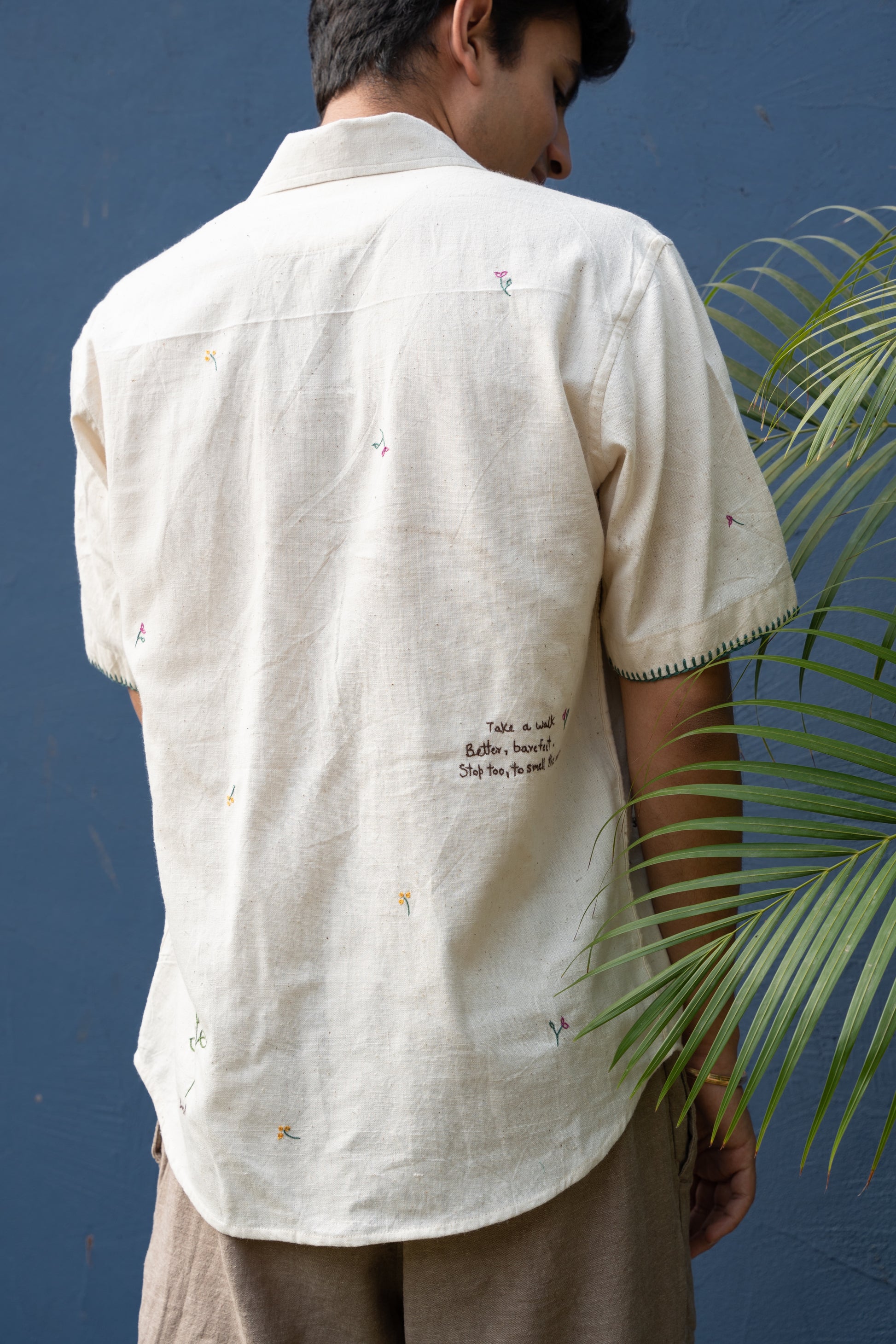 Back of a young man in an off-white half sleeved shirt with a beautiful quote hand-embroidered