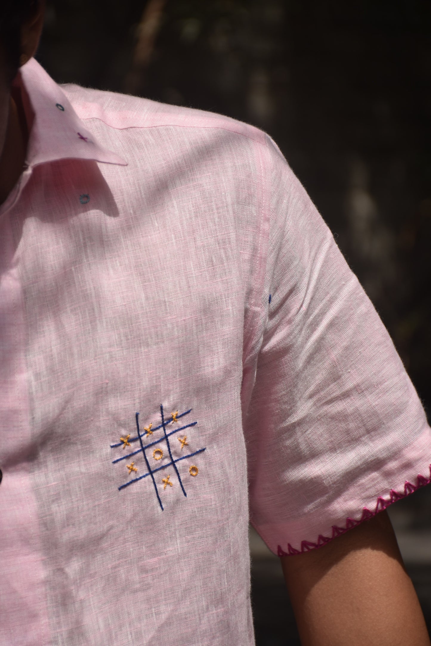 Detail of a pink linen shirt with hand-embroidered tic tac toes