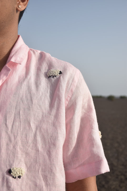 Details of a pink linen shirt with sheep embroidered throughout. The sheep is embroidered with french knot technique