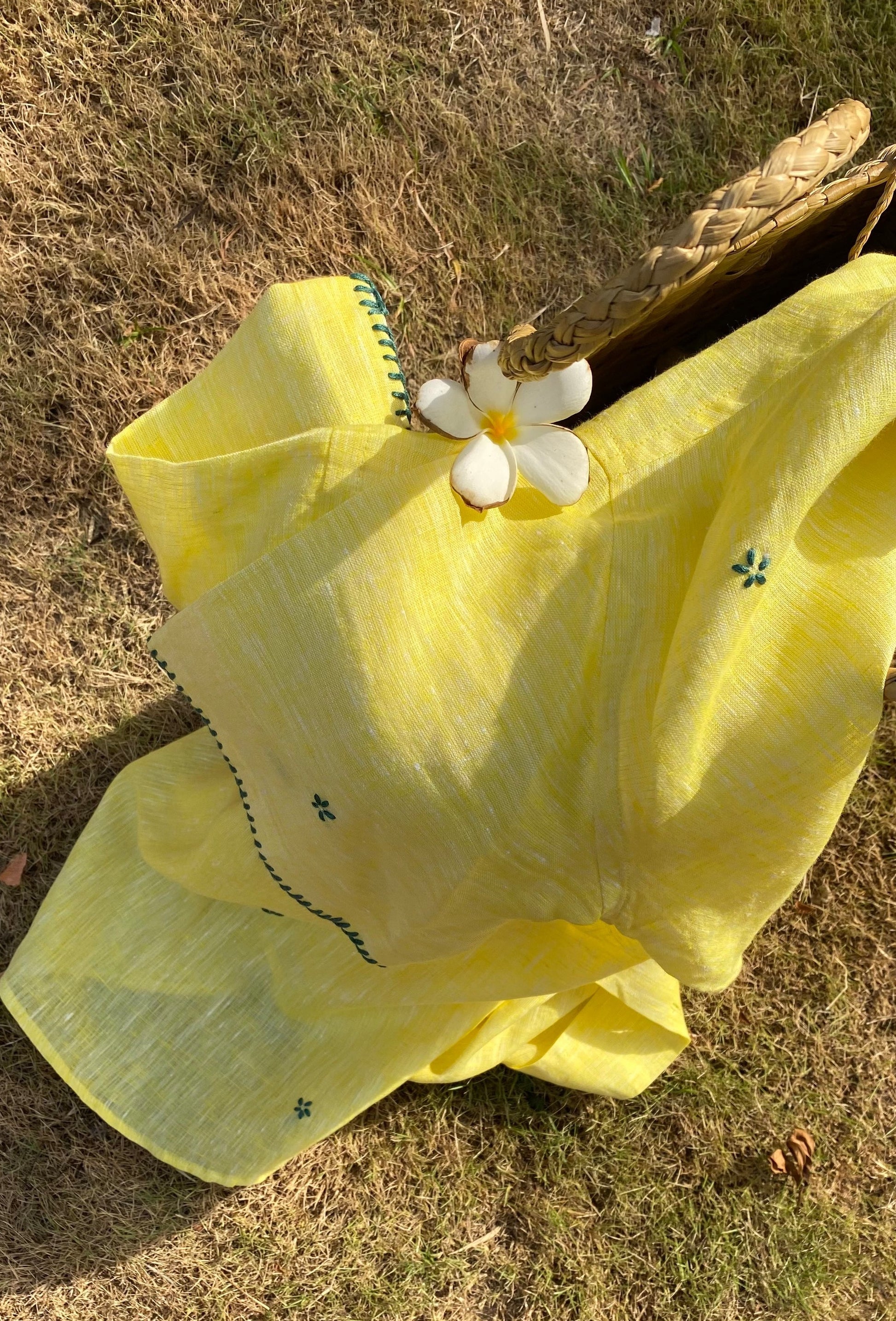 Flatlay picture of a yellow linen shirt with small green flowers embroidered throughout