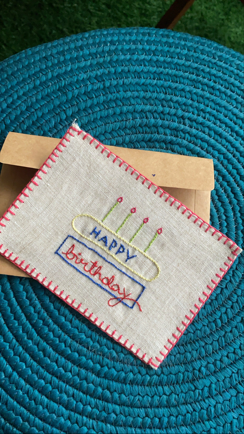 Close-up view showcasing the intricate hand embroidery of a birthday cake on a linen postcard