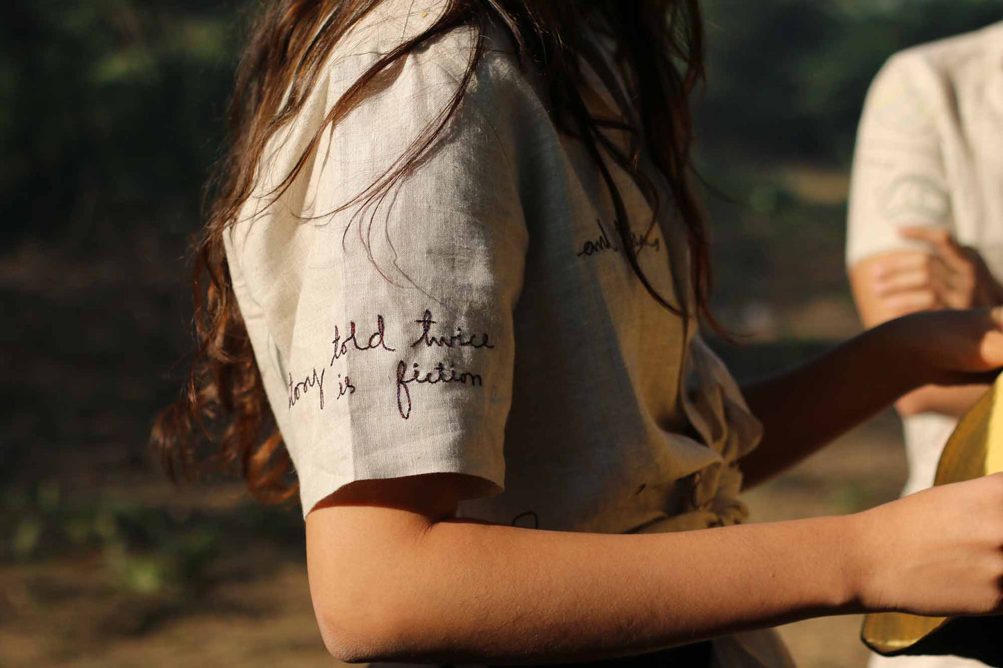 Sleeve details of a beige linen shirt with embroidered texts