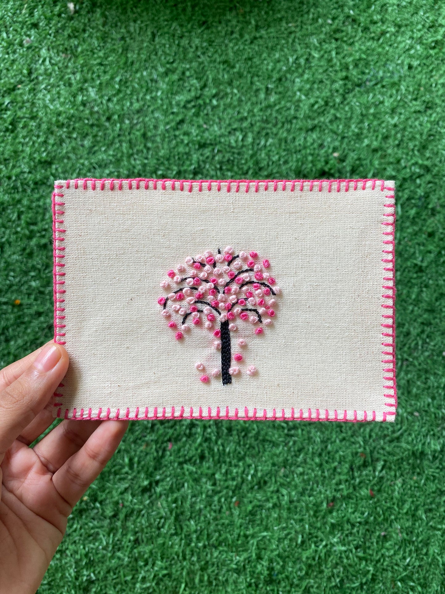 Close-up of the cherry blossom embroidery, showcasing delicate pink and white threads on a linen backdrop