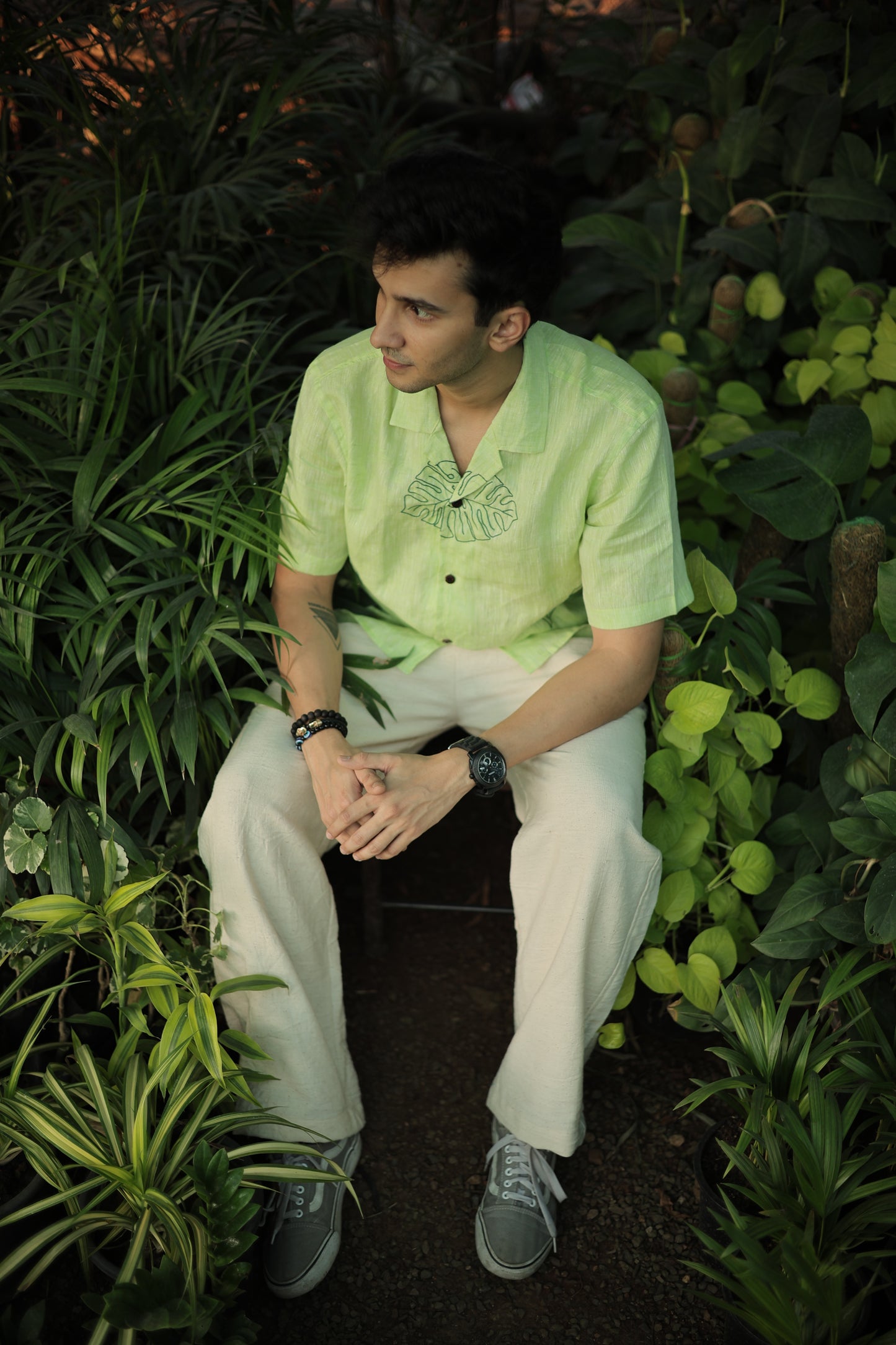 Karan in a green linen shirt with hand embroidered leaves sitting among different plants