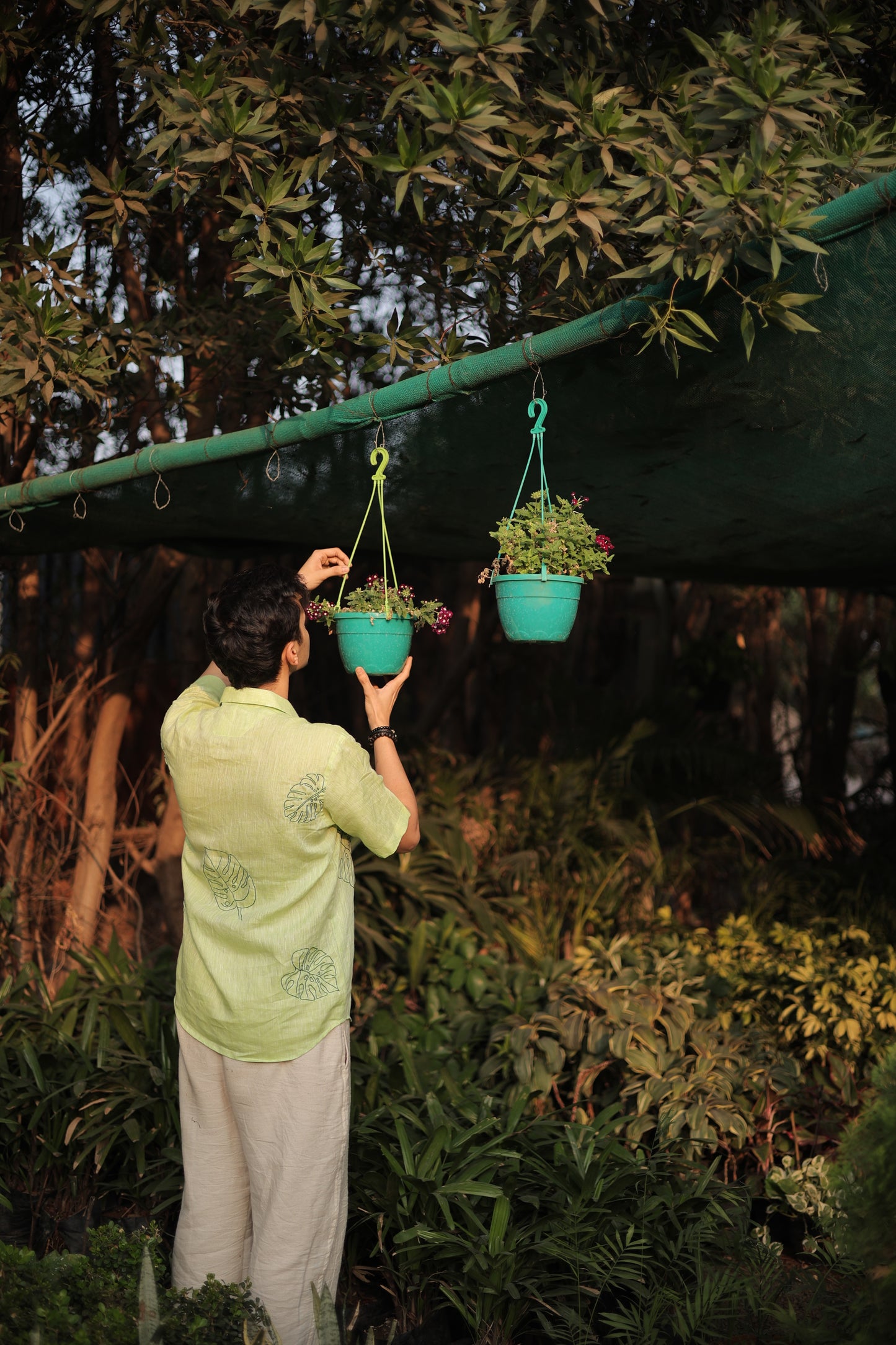 Back detail of a green linen shirt with hand embroidered leaves sitting among different plants