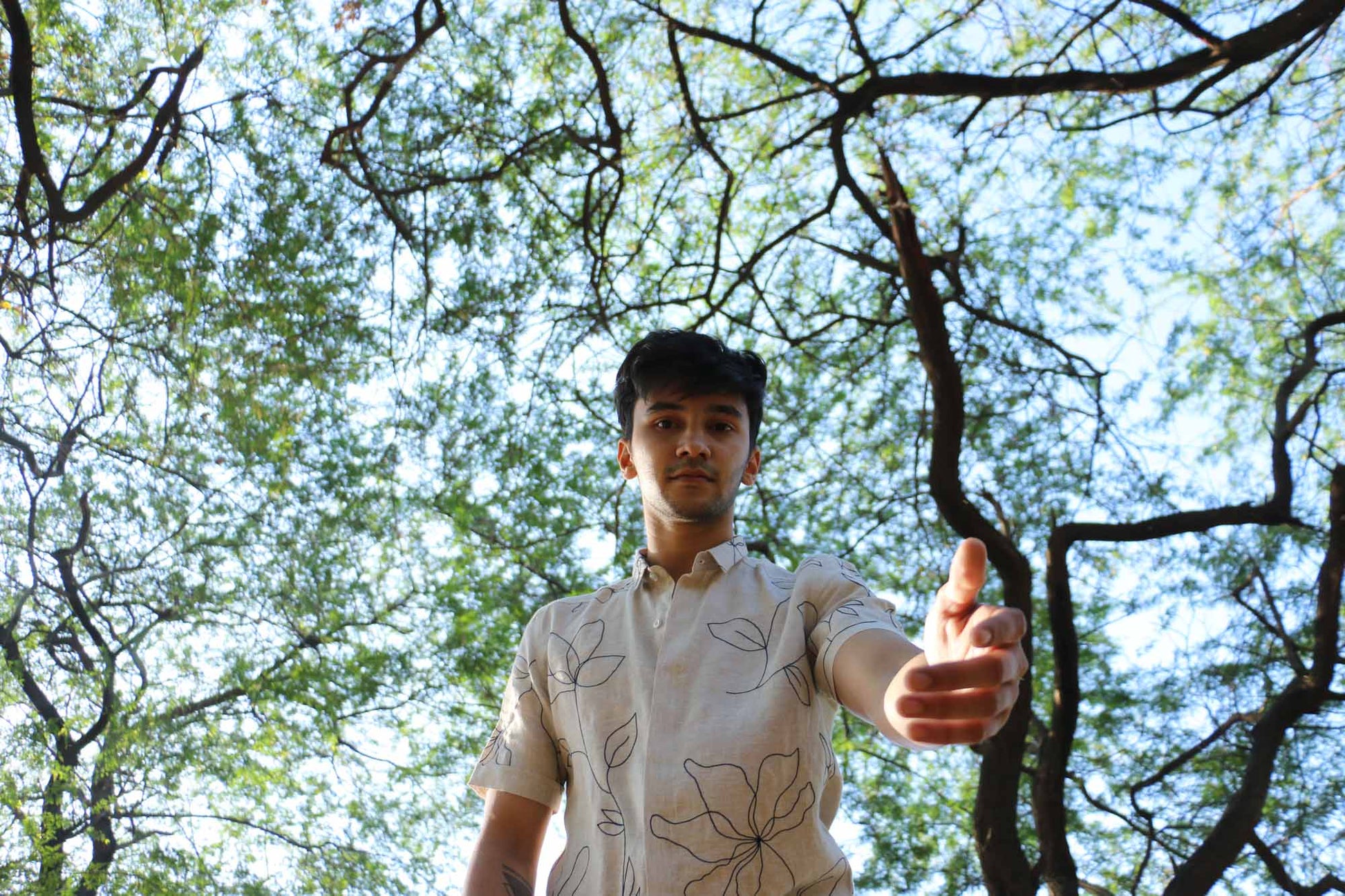 Karan in a half sleeved beige linen shirt is standing in a forest