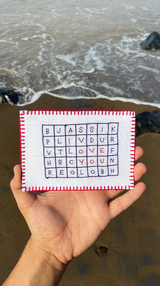 Hand-embroidered postcard displaying 'I Love You' as a crossword puzzle, crafted from sustainable linen, ideal for a unique romantic gesture