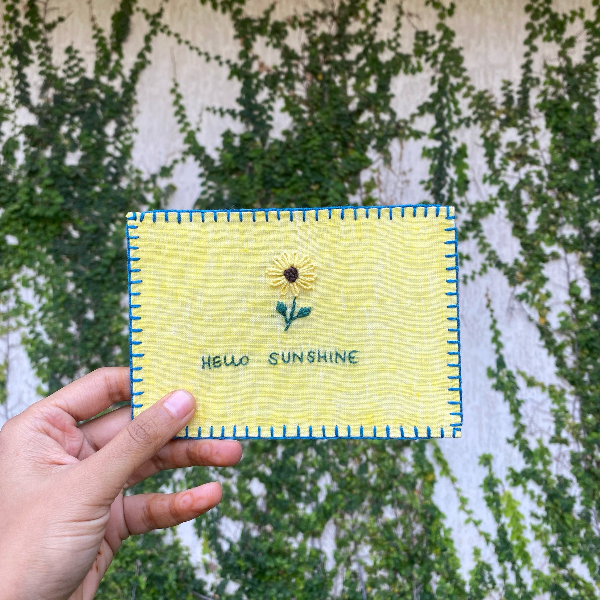 Hand-embroidered postcard showcasing a bright sunflower, symbolizing warmth and positivity, crafted from sustainable linen