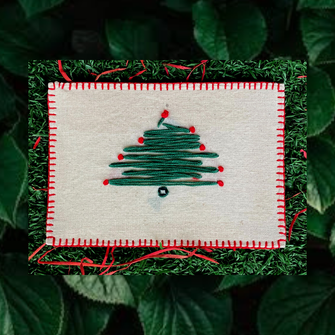 Close-up of intricate hand embroidery featuring a festive Christmas tree on a linen postcard